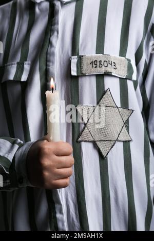 Jüdischer Gefangener mit Marke und brennender Kerze auf schwarzem Hintergrund, Nahaufnahme. Internationaler Holocaust-Gedenktag Stockfoto