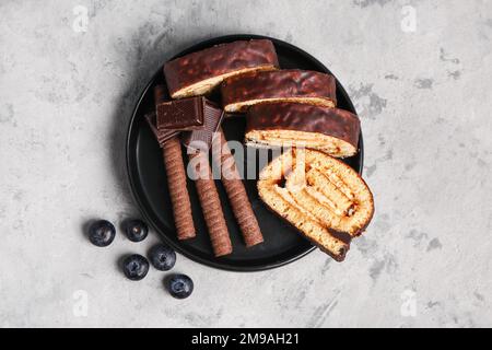Teller mit leckeren Biskuitbrötchen, Schokolade, Waffelbrötchen und Blaubeere auf Grunge-Hintergrund Stockfoto
