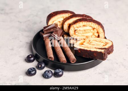 Teller mit leckeren Biskuitbrötchen, Schokolade, Waffelbrötchen und Blaubeere auf Grunge-Hintergrund Stockfoto