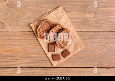 Backpapier mit köstlichen Kuchenrollen und Schokolade auf einem Holztisch Stockfoto