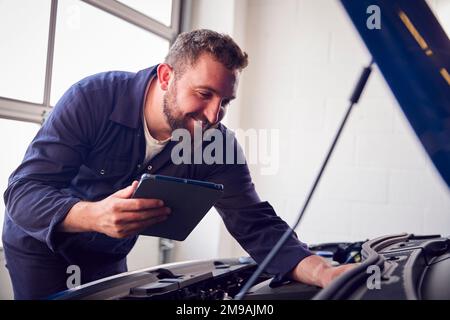 Männlicher Mechaniker In Der Garage, Der Diagnosesoftware Auf Einem Digitalen Tablet Verwendet, Um Den Fahrzeugmotor Zu Warten Stockfoto