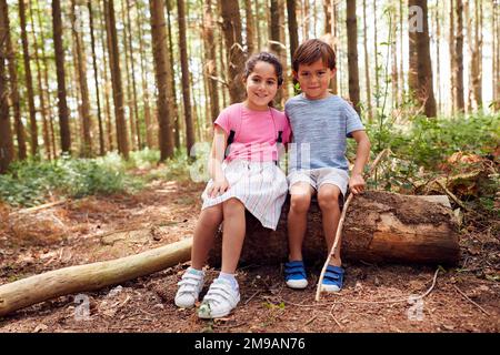 Porträt Von Lächelnden Jungen Und Mädchen, Die In Summer Woodland In Rucksäcken Sitzen Stockfoto