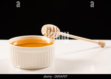 Honig in einer weißen Keramikschüssel mit Holzlöffel, ein Platz für Text auf schwarzem Hintergrund. Linden Honig. Stockfoto