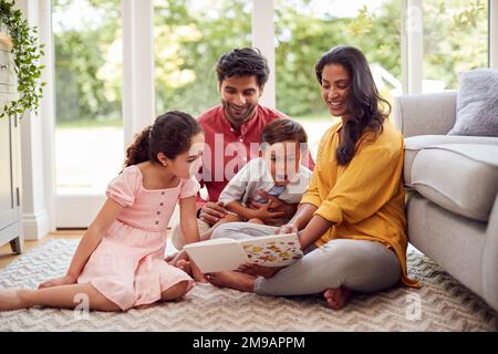 Family At Home Sitzt Auf Der Etage In Der Lounge Und Liest „Book Together“ Stockfoto