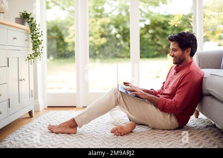 Mann, Der Von Zu Hause Aus Arbeitet Und Auf Der Etage In Der Lounge Mit Einem Laptop Sitzt Stockfoto