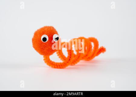 Ausgewählter Fokus auf Kopf Gänsehaut Pfeifenreiniger Wriggly Wurm großer Bommel Bommelkopf lustige Figur Kinderspielzeug Hand isoliert auf weißem Hintergrund Stockfoto