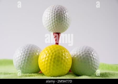 Golfball auf rotem Holzbambus-T-Shirt, umgeben von weißen und gelben Bällen auf einer grünen Teppich-Trainingsmatte Stockfoto