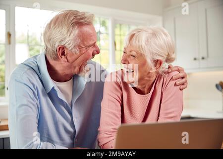 Seniorenpaar, Das Mit Dem Laptop In Der Küche Zu Hause Sitzt Stockfoto