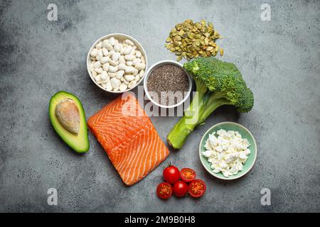 Auswahl gesunder Nahrungsmittel, wenn eine Person Diabetes hat: Lachsfisch, Brokkoli, Avocado, Bohnen, Gemüse, Seeds auf grauem Hintergrund von oben Stockfoto