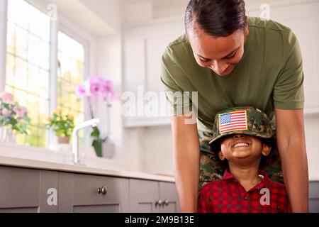 Amerikanische Armee Mutter In Uniform Zuhause Auf Urlaub Mit Sohn Mit Mütze In Der Familienküche Stockfoto