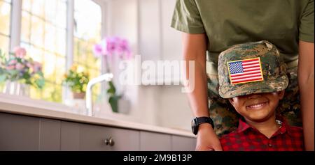 Amerikanische Armee Mutter In Uniform Zuhause Auf Urlaub Mit Sohn Mit Mütze In Der Familienküche Stockfoto
