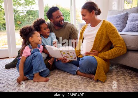 Army Family Mit Schwangerer Mutter, Die Auf Der Etage In Der Lounge At Home Sitzt, Buch Zusammen Lesen Stockfoto