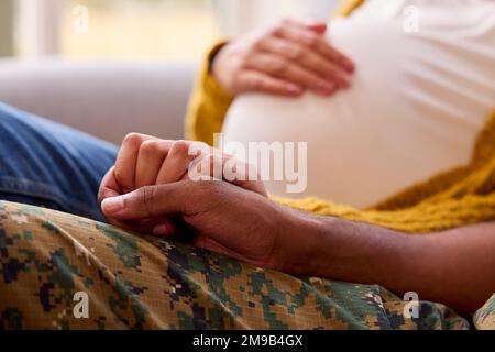 Schwangeres Paar Mit Einer Frau, Die Neben Einem Armeeehemann In Uniform Sitzt Und Hände Nach Hause Hält Stockfoto