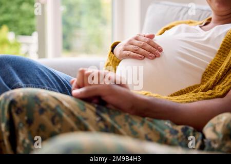 Schwangeres Paar Mit Einer Frau, Die Neben Einem Armeeehemann In Uniform Sitzt Und Hände Nach Hause Hält Stockfoto