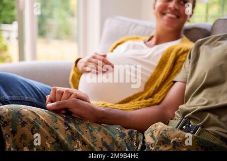 Schwangeres Paar Mit Einer Frau, Die Neben Einem Armeeehemann In Uniform Sitzt Und Hände Nach Hause Hält Stockfoto
