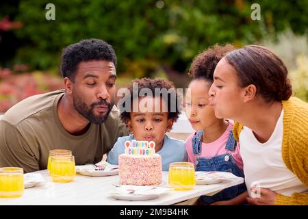 Die Familie feiert den Geburtstag des Kindes in Garden At Home und bläst Kerzen auf Kuchen aus Stockfoto