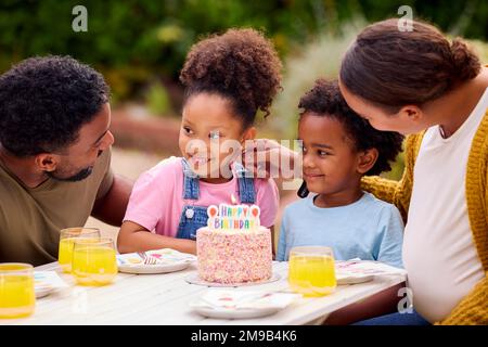 Die Familie feiert den Geburtstag des Kindes in Garden At Home und bläst Kerzen auf Kuchen aus Stockfoto