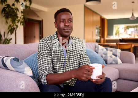 Porträt Von Mann, Der Sich Auf Dem Sofa Zu Hause Mit Einem Heißgetränk Entspannt Stockfoto