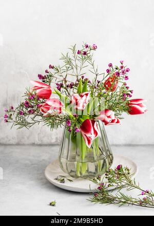 Wunderschöner Strauß aus pinkfarbenen, weißen Tulpen und violetten Wachsblüten in der alten alten Glasvase. Frühlingsblütenanordnung. Stockfoto