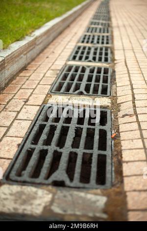 Sturmabfluss für die Wasserableitung. Details der städtischen Kommunikation. Luken des Kanals. Rost auf der Straße. Abfluss für Regenwasser. Stockfoto