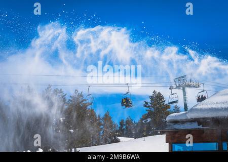 Schneekanone, die frisches Schneepulver auf einer Skipiste ausstreut. Skifahrer fahren mit dem Sessellift. Skiurlaub im Winter in El Tarter, Andorra, Pyrenäen Stockfoto