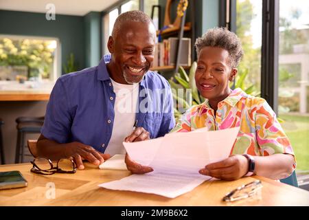 Lächelndes Seniorenpaar, Das Zu Hause Am Tisch Sitzt Und Die Finanzen Prüft Stockfoto