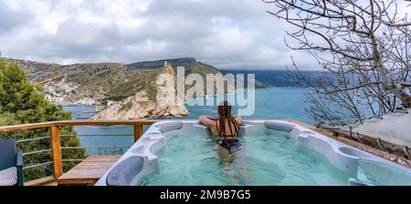 Nehmen Sie sich Zeit für sich. Badesachen im Freien mit Blick auf die Berge und das Meer. Eine Frau im schwarzen Badeanzug entspannt sich im Hotelpool und bewundert die Aussicht Stockfoto