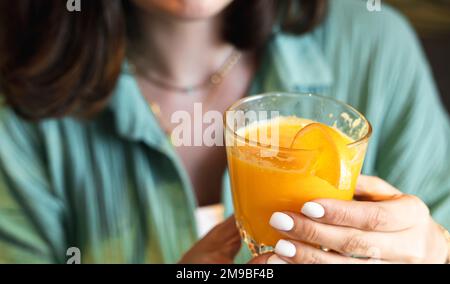 Mädchen trinkt frisch gepressten Orangensaft durch Stroh in Glas. Helles Hipster-Frühstücksrestaurant, Café. Gesundes Essen. Veganer, Vegetarier dr. Stockfoto