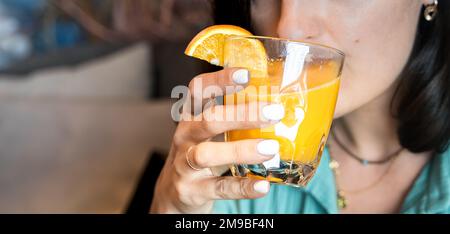 Mädchen trinkt frisch gepressten Orangensaft durch Stroh in Glas. Helles Hipster-Frühstücksrestaurant, Café. Gesundes Essen. Veganer, Vegetarier dr. Stockfoto