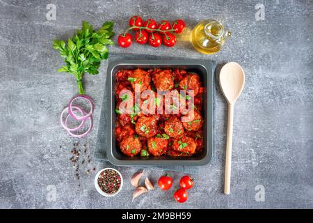 Hausgemachte Fleischbällchen mit Tomatensoße und Gewürzen, serviert in schwarzer Pfanne auf grauem Betonhintergrund. Leckere gekochte Fleischbällchen mit Hackfleisch und Foo Stockfoto