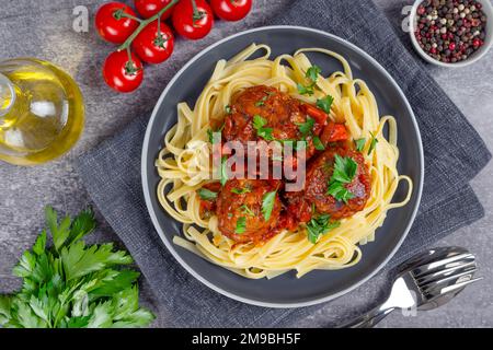 Hausgemachte Spaghetti mit Tomatensoße, Fleischklößchen und Gewürzen, serviert auf schwarzem Teller auf grauem Betonhintergrund. Leckere gekochte Pasta mit Hackfleisch Stockfoto