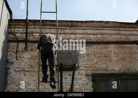 Ein Mann klettert auf die Leiter auf das Dach. Eine Person klettert die Treppe hoch. Abstieg vom Dach. Der Mann hält sich am Geländer fest. Stockfoto