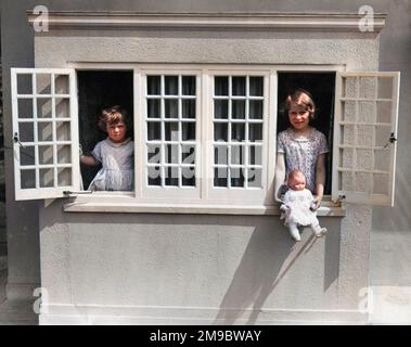 Bezauberndes Foto von Prinzessin Elizabeth (Königin Elizabeth II) und ihrer jüngeren Schwester Prinzessin Margaret, die an den Fenstern von y Bwthyn bach to Gwellt (das walisische Cottage) posiert, einem Spielzeughaus, das Prinzessin Elizabeth zum sechsten Geburtstag von den Menschen von Wales geschenkt wurde. Stockfoto