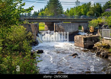 Eine Straßenbrücke über einen kleinen Fluss und einen gebrochenen Damm in den Laurentians, Quebec, Kanada. An einem sonnigen Sommernachmittag ohne Leute aufgenommen. Stockfoto