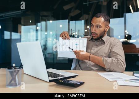 Ein unzufriedener Geschäftsmann zeigt ein Diagramm mit schlechten Erfolgen in der Kamera an. Ein lateinamerikanischer Mann berichtet bei einem Online-Meeting von Firmenmanagern, einem Mann bei der Arbeit, über negative Ergebnisse. Stockfoto