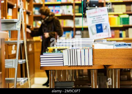 Abstrakte Buchhandlung, Stapel Bücher auf dem Tisch. Unerkennbare Silhouette älterer Frauen bei der Buchwahl Stockfoto