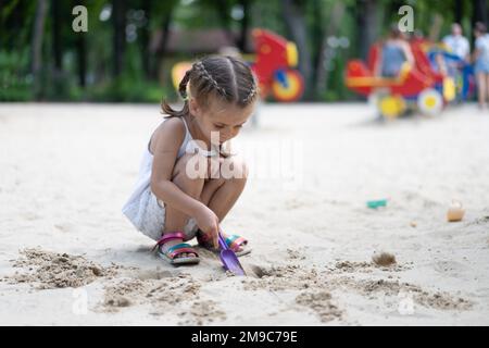 Kleines Mädchen Spielt Sandbox Spielplatz Graben Sand Schaufel Gebäude Sandfigur Sommertag. Kaukasische weibliche Kind 5 Jahre haben Spaß im Freien Stockfoto