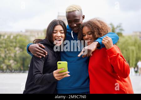 Multi ethnische Freunde im Freien suchen Smartphone-Bildschirm. Diverse Gruppe Menschen Afro american Asian verbringen Zeit zusammen multirassischen männlichen weiblichen Studenten Treffen im Freien Stockfoto