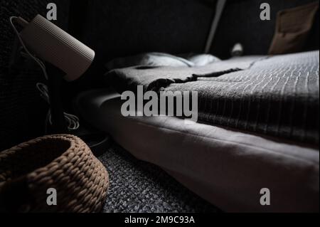 Doppelbett auf Teppichboden im Schlafzimmer der Holzkabine. Pyramidenförmiger Bungalow. Kleines Zimmer, abgewinkelte Wände, Fensterbeleuchtung, Bett, Nachtlampe und Knitte Stockfoto