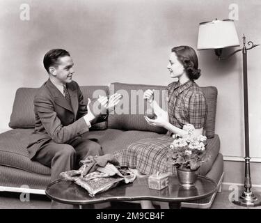 1940S LÄCHELNDES, JUNGES PAAR, DAS ZUSAMMEN AUF DER COUCH IM WOHNZIMMER SITZT, MANN IM ANZUG, DER FRAU HILFT, EINEN BALL AUFZUZIEHEN WOLLGARN - J8180 HAR001 HARS COUCH KOMMUNIKATION JUNGER ERWACHSENER BALANCE TEAMARBEIT FREUDE LEBENSSTIL FRAUEN HOME LIFE WOLLE COPY SPACE FRIENDSHIP DURCHGEHENDE, HALBE LÄNGE, DAMEN, MÄNNER, TEENAGER, JUNGE, CRAFT-UNTERHALTUNG, BASTELGARN, ERFOLG WEITWINKEL VERFÜHRERANZUG UND KRAWATTE GLÜCK FRÖHLICHE FREIZEITSTRATEGIE WOHNZIMMER ERHOLUNGSSTOLZ SICH AUF ATTRAKTION LÄCHELN VERBINDUNG BEGEISTERUNG KONZEPTIONELL FRÖHLICH STILVOLLE SKEIN-MÖGLICHKEIT KOOPERATION ENTSPANNUNG Stockfoto