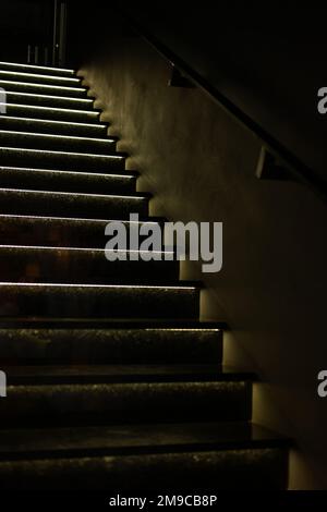 Treppenhaus, Notausgang in einem Wohnblock. Treppe im Innenbereich, Feuerleiter, gegen graue Betonwände auf und ab mit natürlichem Sonnenlicht von der Tür Stockfoto