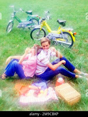 1970S PICKNICK-PAAR MIT MOPEDS, DAS IM GRAS SITZT, RÜCKEN AN RÜCKEN KORB MIT BROTFRUCHTKÄSE UND BLUE JEANS SOFT TRÄGT FOCUS - KC8124 PHT001 HARS WEICHE JUNGE ERWACHSENE BAUMWOLLE ZUFRIEDEN LEBENSSTIL ZUFRIEDENHEIT FRAUEN LÄNDLICHE GESUNDHEIT KOPIER WELTRAUM FREUNDSCHAFT VOLLE LÄNGE DAMEN PERSONEN MÄNNER DENIM SCHWERPUNKT TRANSPORT DATIEREN GLÜCK FRÖHLICH HOCHWINKEL ABENTEUER ATTRAKTION LÄCHELT AL FRESCO VERBINDUNG BALZSCHAFT FLUCHT FREUDIG PICKNICK STILVOLL BLAUE JEANS ZWANGLOSE MOPEDS SOZIALE AKTIVITÄT ZUSAMMENSEIN JUNGER ERWACHSENER MANN JUNGE ERWACHSENE FRAU RÜCKEN AN RÜCKEN ZWANGLOSE, KAUKASISCHE ETHNIZITÄT Stockfoto