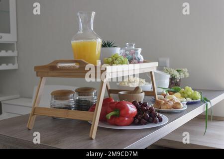 Köstliches Frühstück mit Orangensaft, Tee, Obst, Beeren, Gemüse und Croissants auf einem Holztisch in skandinavischem Interieur. Stockfoto
