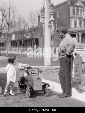 1920S LÄCHELNDES KLEINES MÄDCHEN, DAS NEBEN IHREM TRETWAGEN STEHT UND MIT EINEM HUND NACH BENZIN FRAGT, VON EINEM AFROAMERIKANISCHEN TANKWART. M2303 HAR001 HARS NOSTALGIA ALTMODISCH AUTO 1 ALBERNER SITZ JUGENDLICHER KOMMUNIKATION FAHRZEUG COMIC SCHLAUCH FREUDEN LIFESTYLE PUMPS FRAUEN ERWACHSENENTRANSPORT KOPIERRAUM MENSCHEN KINDER FREUNDSCHAFT VOLLE LÄNGE FRAGEN PERSONEN ERWACHSENE AUTOS MÄNNER TRETTRANSPORT B&W HUMORVOLL GLÜCK SÄUGETIERE FRÖHLICH ABENTEUER KREUZUNG TANKSTELLE KUNDENSERVICE AFROAMERIKANER AFROAMERIKANER DÜSENKANINCHEN ERHOLUNG SCHWARZ ETHNISCH KOMISCHE ZAPFSÄULE STOLZ BESETZUNGEN Stockfoto