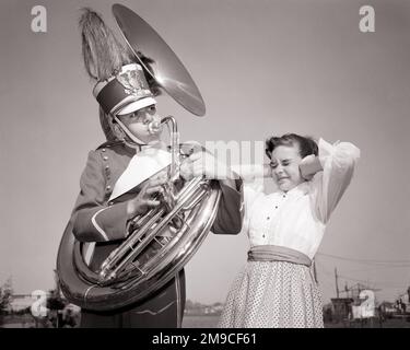 1950S TEENAGER, DER LAUT TUBA SPIELT UND BANDUNIFORM TRÄGT UND EIN JUNGES MÄDCHEN, DAS DIE HÄNDE ÜBER DIE OHREN HÄLT THE NOISE - M2305 DEB001 HARS KOMMUNIKATIONSFREUND COMIC NOISE LIFESTYLE SOUND ZUFRIEDENHEIT MUSIKERIN VERÄRGERTE WEIBLICHE BRÜDER KOPIEREN WELTRAUMFREUNDSCHAFT INSPIRATION IN HALBER LÄNGE MÄNNCHEN TEENAGER JUNGE BRASS GESCHWISTER B&W HUMORVOLL UND AUFREGEND LAUTER LOW-ANGLE-FREIZEITVERGNÜGEN KOMISCHER STOLZ GESCHWISTERMUSIK INSTRUMENT TUBA VERBINDUNG KONZEPTIONELLE KOMÖDIE FREUNDLICHE UNTERSTÜTZUNG DEB001 ÄRGERNIS WACHSTUM JUGENDLICHE LAUTE GERÄUSCHE KINDER VOR TEENAGER JUNGE VOR TEENAGER MÄDCHEN EIN JUGENDLICHER Stockfoto