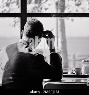 1960S 1970S ANONYMER MANN MIT SILHOUETTE, DER AUF DEM KAFFEETISCH SASS, MIT EINER KAFFEETASSE, DIE ZIGARETTE RAUCHTE UND AUS DEM FENSTER BLICKTE, IN GEDANKEN VERLOREN - S17246 HAR001 HARS B&W TRAURIGKEIT CAFÉ ZIGARETTEN DACHTE ANGST TRÄUME KOPF UND SCHULTERN TABAK STRATEGIE SILHOUETTED REFLEKTIEREND DENKEN VERZWEIFLUNG RÜCKBLICK SCHLECHTE ANGEWOHNHEIT REFLEKTIERT RAUCHER PSYCHISCHE GESUNDHEIT NIKOTIN-DENKEN VERLOREN IN GEDANKEN TASSE KONZEPTIONELL VON HINTER SÜCHTIG FANTASIE GEDANKEN ÜBER DIE ANONYME MEDITATION RÜCKBLICK IDEEN MEDITATIVE JUNGE ERWACHSENE MANN SCHWARZ-WEISS WEISS WEISSE ETHNISCHE ZUGEHÖRIGKEIT BETRACHTET HAR001 MENTALE KRANKHEIT ALTMODISCH Stockfoto