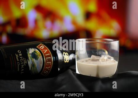 KIEW, UKRAINE - 4. MAI 2022 Baileys Original-Alkoholflasche auf Holztisch mit rotem Kamin im Hintergrund. Elite-Alkoholproduktion Stockfoto