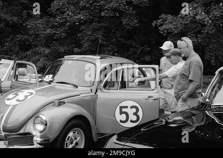 Drei Männer inspizieren einen alten Volkswagen-Käfer, der als Herbie der Liebeskäfer auf einer Autoausstellung in Essex, Massachusetts, gemalt wurde. Das Bild wurde in Schwarz aufgenommen Stockfoto