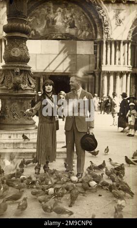 Ein Paar umgeben von Tauben auf dem Markusplatz in Venedig. Stockfoto