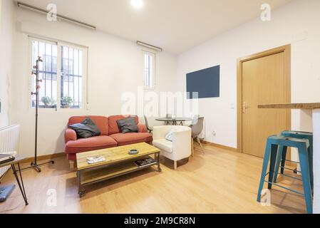 Apartment im Loft-Stil mit einer Kiefernholztheke mit blauen Metallhockern und einem Zweisitzer-Sessel mit einem Couchtisch im Industriedesign Stockfoto